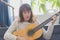 Beautiful young woman sitting on sofa playing guitar