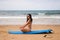 Beautiful young woman sitting on the surfboard on the shore of the beach. The woman is enjoying her trip to a paradise beach.