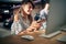 Beautiful young woman sitting at table in front of desktop computer using smartphone, feeling joyful