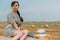 Beautiful young woman sitting on top of bale in the middle of wheat field with bales in summer evening