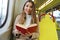 Beautiful young woman sitting in tram caught and surprised at reading her book looks at camera