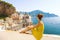 Beautiful young woman sitting on wall looking at stunning panoramic village of Atrani on Amalfi Coast, Italy