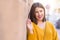 Beautiful young woman smiling confident and cheerful leaning on bricks wall, walking on the street of the city on a sunny day