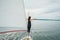 Beautiful young woman standing on the bow of a sail boat on a tranquil calm blue sea