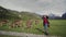 Beautiful young woman stands next to alpine cows in a pasture and smiling, feels happy, makes horns on her head with