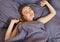 Beautiful young woman stretching after waking up while in cozy bedroom bed, smiling rested girl feeling refreshed sitting on white