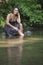 Beautiful young woman in sundress sitting by creek - rural summer