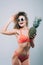 Beautiful young woman in sunglasses with perfect body wearing bikini holding a pineapple isolated on the gray background
