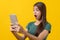 Beautiful young woman surprised facial expression after seeing shocking, amaze deal in mobile phone isolated on yellow background.