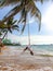 Beautiful young woman swinging on the rope tied to coconut palm on the ocean beach