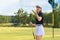Beautiful young woman is throwing up a golf ball while standing on golf course.