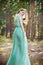 Beautiful young woman in a turquoise dress in a pine forest