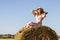 Beautiful young woman in vintage pink dress sitting on hay bale. Life in countryside concept.