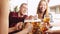 Beautiful young woman, waitress serving big mugs with lager beer to group of young people, friends meeting together at