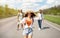 Beautiful young woman walking along highway with her male friends, having summertime journey, backpacking outdoors