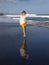 Beautiful young woman walking on black sand beach. Caucasian woman wearing yellow sportswear and white blouse. Happiness