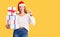 Beautiful young woman wearing christmas hat and holding a gift surprised with an idea or question pointing finger with happy face,