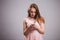 Beautiful young woman wears pink dress and uses smartphone on grey background with copy space