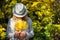 Beautiful young woman in white clothes and hat tilted her head to the bouquet of yellow leaves in her hands. Elegant blonde, face