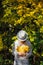 Beautiful young woman in white clothes and hat tilted her head to the bouquet of yellow leaves in her hands. Elegant blonde, face