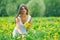 Beautiful young woman in a white dress collects dandelions on a green meadow