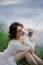 Beautiful young woman in white dress resting on shore lake pond river. Professional makeup and hairstyle with curled hair