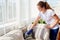 Beautiful young woman in white shirt and jeans cleaning sofa with vacuum cleaner in living room, copy space. Housework.