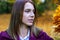 Beautiful young woman in a white shirt and purple coat looks at a bouquet of dry yellow leaves.