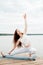 Beautiful young woman in white sports clothes in warrior yoga pose on  wooden pierce on lake outdoor