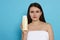 Beautiful young woman wrapped in towel holding bottle of shampoo on light blue background. Space for text