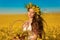 Beautiful young woman with wreath on long healthy hair over Yellow rape field landscape background. Attracive brunette girl with