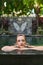 Beautiful zen woman relaxing outdoors in lush and modern stone swimming pool of luxurious hotel during tropical travel