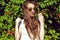 Beautifull woman with long chestnut hair blown by the wind in mirrored sunglasses standing at the creeper hedge