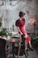 Beautifull young woman stands turned back against grey wall in red dress near served table with candles and fir branches