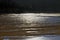 Beautifully patterened wet sand reflecting blue sky silhouetted by dark cliffs