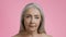 Beauty of aging. Close up portrait of beautiful senior grey haired wrinkled lady looking to camera, pink background