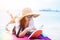 Beauty Asian woman have vacation on beach. Girl wearing wing hat and reading book on colorful mat near sea. Lifestyle and happy