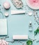 Beauty background with facial cosmetic products, shopping bag and twigs with cherry blossom on pastel blue desktop background.