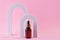 Beauty collagen face serum in a glass dropper bottle in Arch on pink background. Trendy shoot of cosmetics packaging. Essential