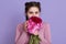 Beauty delicate woman smelling spring flowers and looking directly at camera with charming expression, lady with pigtails holding