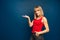 Beauty fashion portrait of slim blonde woman in red shirt on a blue background in studio showing on a place near her. Copyspace