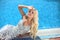 Beauty fashion smiling blond girl model posing in party dress lying near swimming pool. Luxury life. Resort. Summer Vacation.