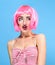 Beauty head shot. Surprised Young woman with creative pop art make up and pink wig looking at the camera on blue background