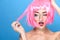 Beauty head shot. Young woman with creative pop art make up and pink wig looking at the side on blue background