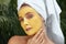 Beauty Mask. Woman In Bath Towel On SPA Procedure Close Up Portrait. Face Covered With Yellow Skin Care Product.