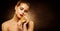 Beauty Model with Golden Makeup holding Gold Jewelry. Face Skin Care and Luxury Cosmetics. Shining Glitter Dark Background
