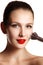 Beauty model with makeup Brush. Bright make-up for brunette woman with blue Eyes. Red lips. Beautiful Face. Perfect Skin.