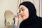 Beauty muslim woman with hijab applying makeup. Beautiful girl looking in the mirror and applying cosmetic. Girl gets