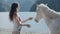 Beauty and nature concept. Pregnant woman petting white horse by the mountain lake at beautiful sunlight. Unity of human