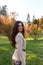 Beauty portrait of a cheerful brunette girl with long curly hairstyle in elegant fall outfit in the park